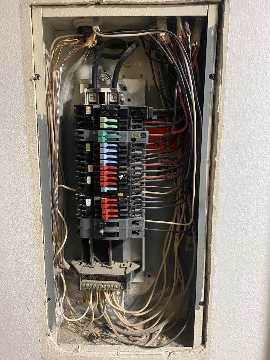 An open electrical panel set into a wall, with rows of breakers and neatly dressed wires.