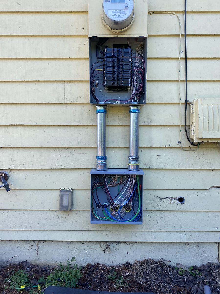 After: the same wall with two metal conduits running from the panel down into a new gray junction box.