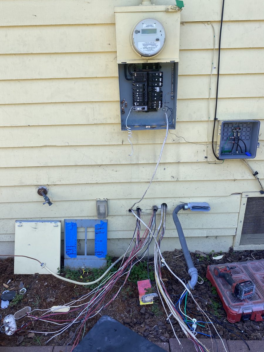 Before: loose, multicolored wires hanging out of yellow siding below an electric meter and panel, trailing into the dirt next to an open tool box.